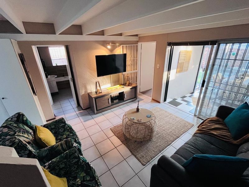 A cozy living room featuring exposed ceiling beams, tiled flooring, and direct access to an outdoor patio area through sliding glass doors.