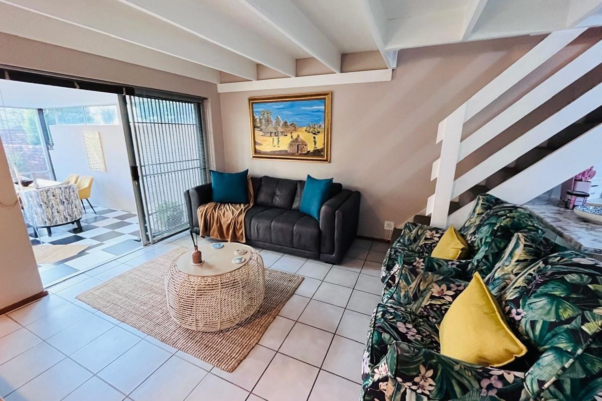 A living room featuring exposed ceiling beams, tiled flooring, and a staircase, with a sliding glass door providing access to an outdoor patio area.