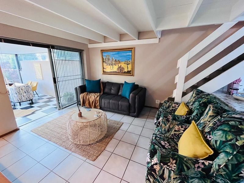 A living room featuring exposed ceiling beams, tiled flooring, and a staircase, with a sliding glass door providing access to an outdoor patio area.