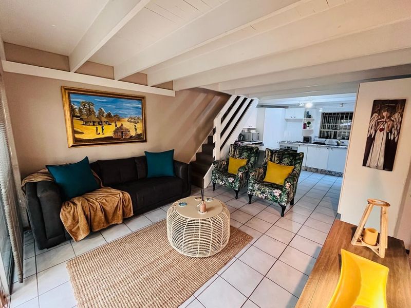 Open-plan living area featuring tiled floors and exposed beam ceilings, seamlessly flowing into a functional kitchen space with built-in cabinetry and appliances.