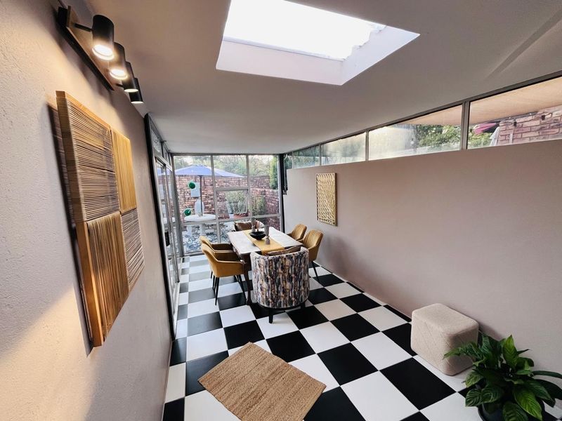 A bright, enclosed patio area featuring a skylight, modern track lighting, and distinctive checkerboard tile flooring with direct access to the garden.