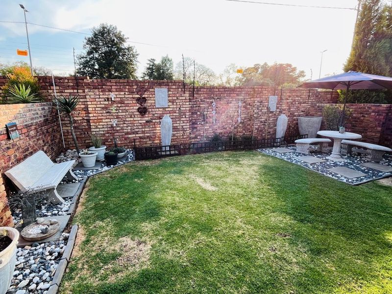 A private rear garden featuring a well-maintained lawn, decorative pebble borders, and a secure brick boundary wall with integrated electric fencing.