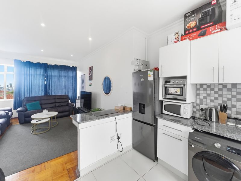 Open-plan living area featuring a compact kitchen with granite countertops, mosaic backsplash, and integrated appliances, flowing into a comfortable lounge space.