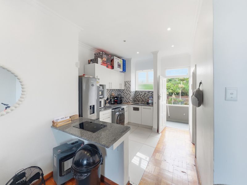 A functional kitchen featuring built-in cabinetry, granite countertops, a hob, and a mix of parquet and tiled flooring, with direct access to a balcony.