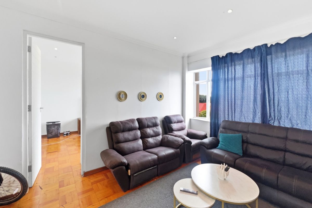 A bright living room featuring classic parquet flooring, recessed downlighting, and neutral wall finishes, providing a comfortable and well-maintained living space.