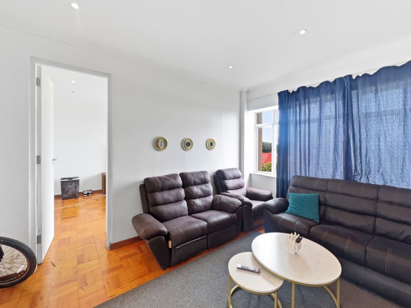 A bright living room featuring classic parquet flooring, recessed downlighting, and neutral wall finishes, providing a comfortable and well-maintained living space.