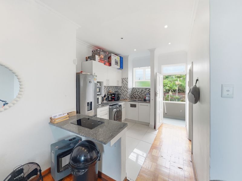 A functional kitchen featuring granite countertops, an integrated electric hob, tiled backsplash, and a mix of tiled and parquet flooring with direct outdoor access.