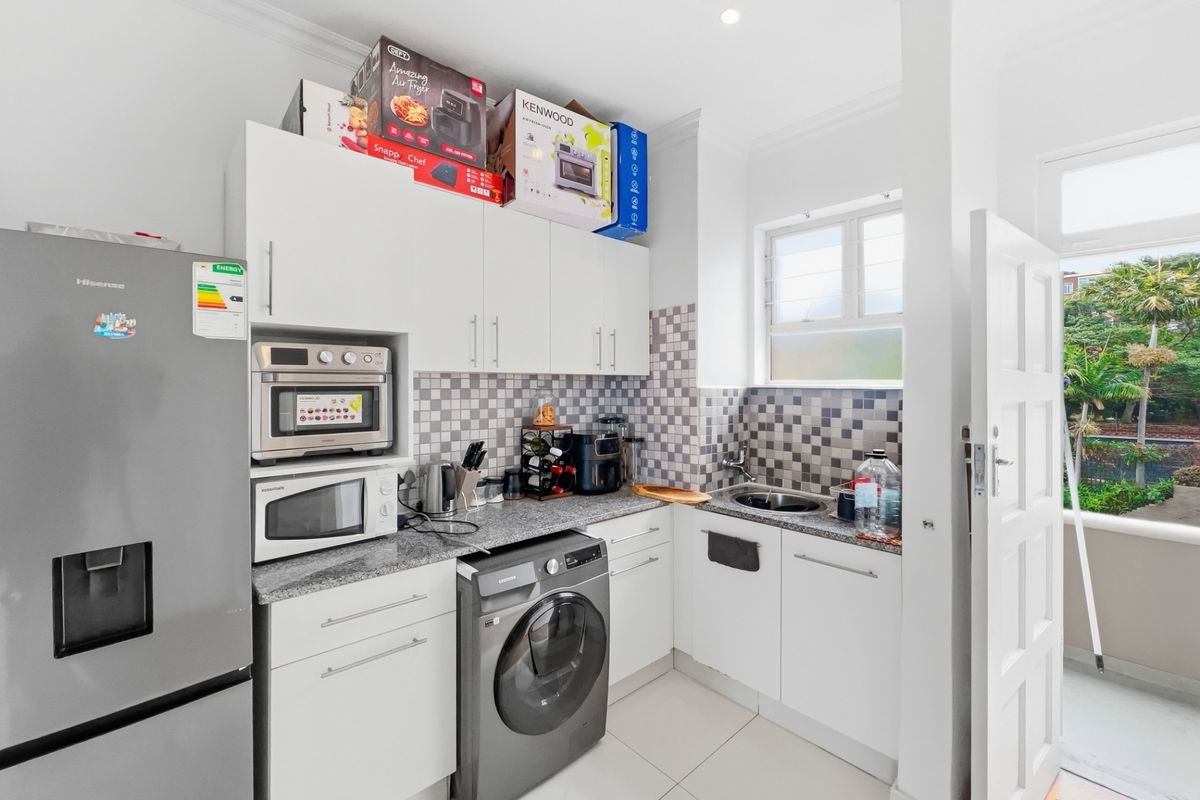 Compact kitchen featuring white cabinetry, granite countertops, mosaic tile backsplash, and integrated microwave, with direct access to an outdoor balcony area.