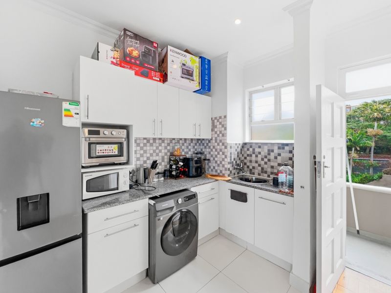 Compact kitchen featuring white cabinetry, granite countertops, mosaic tile backsplash, and integrated microwave, with direct access to an outdoor balcony area.