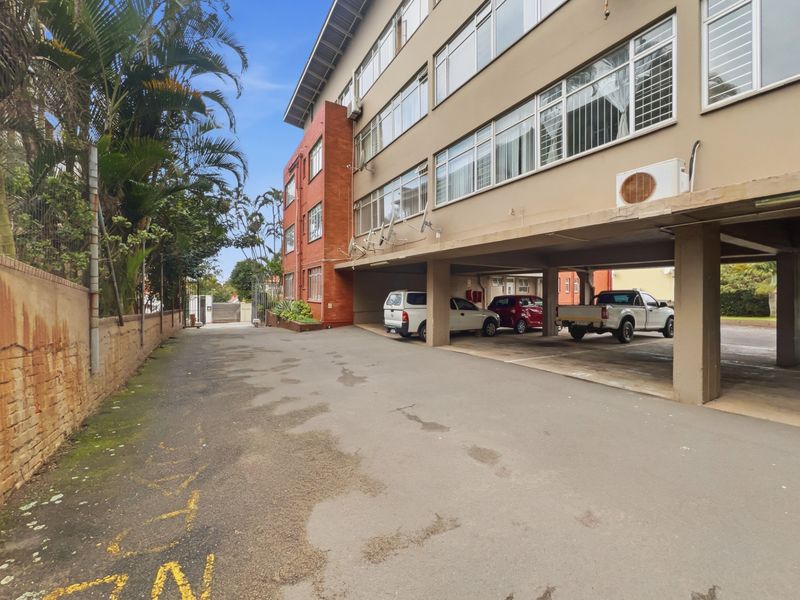 Exterior view of the apartment building featuring a covered parking area, brick and rendered facade, and secure gated access.