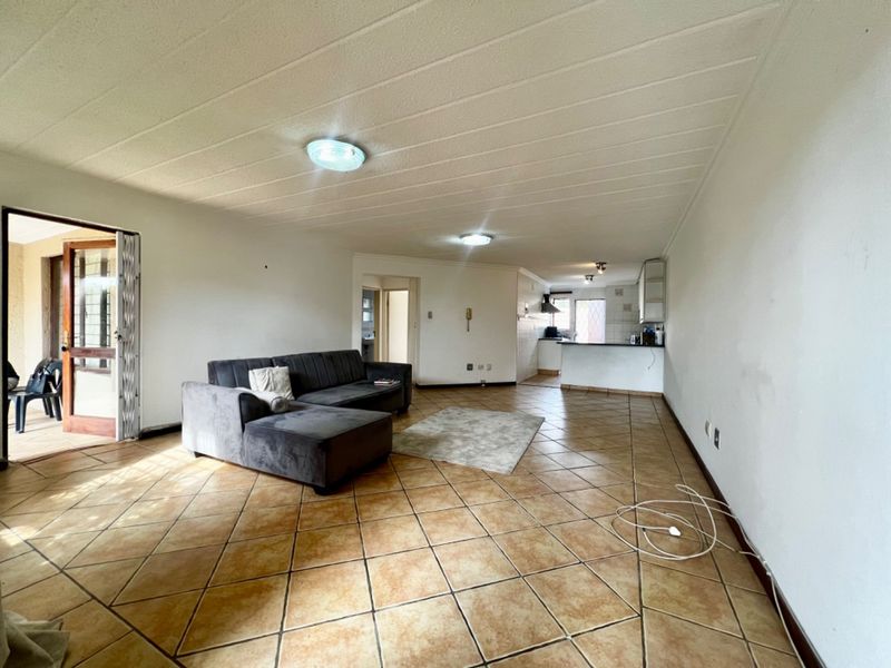 Spacious open-plan living area featuring ceramic tile flooring, a functional kitchen with breakfast bar, and direct access to an outdoor patio area.