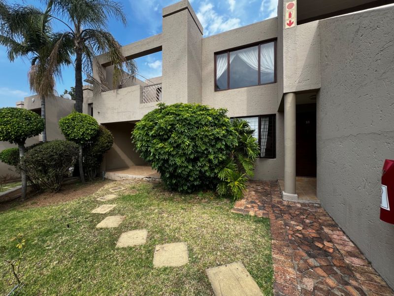 Front elevation of a multi-story apartment unit featuring a textured facade, private balcony, stone walkway, and established garden area.