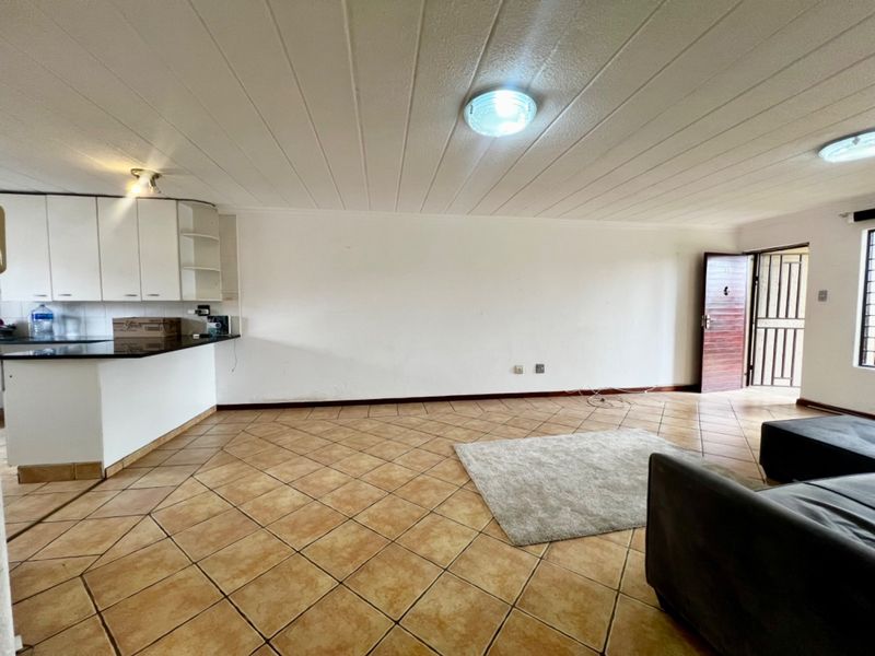Open plan living area featuring tiled flooring, built-in kitchen cabinetry with granite countertops, and direct access to a secure entrance.