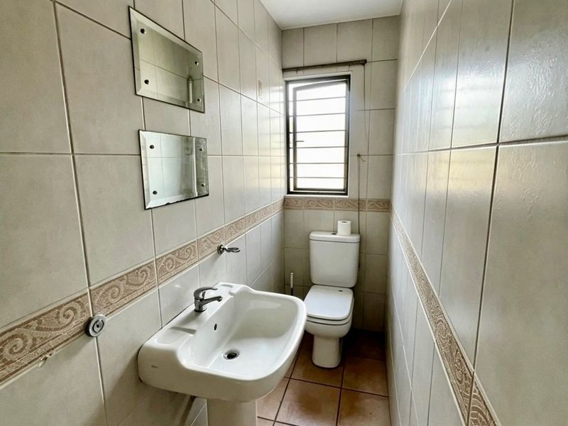 A compact bathroom featuring a pedestal basin, toilet, and neutral ceramic wall and floor tiling with decorative border accents.