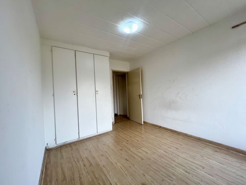 An empty bedroom featuring laminate flooring, built-in cupboards, and a ceiling with tiles. The room requires cosmetic updates to the walls and finishes.