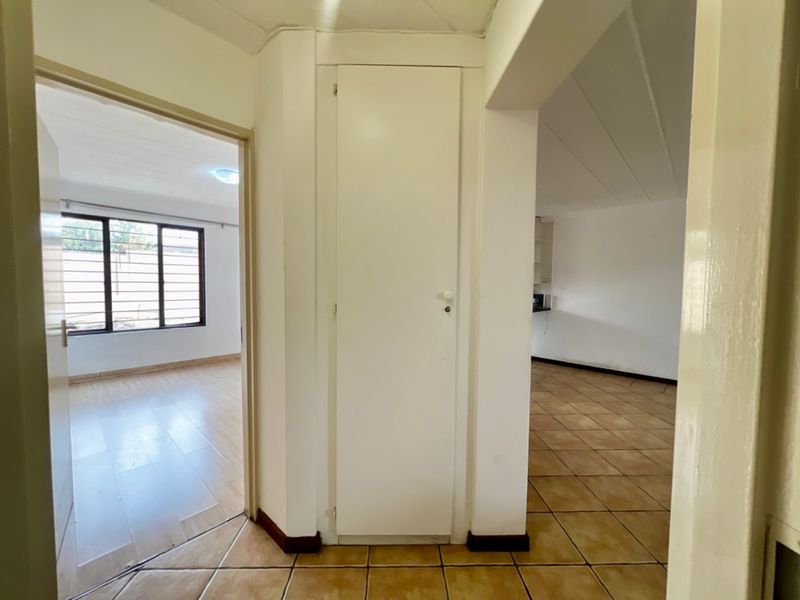 A functional hallway area featuring tiled flooring and a built-in storage cupboard, providing access to adjacent living spaces and bedrooms.