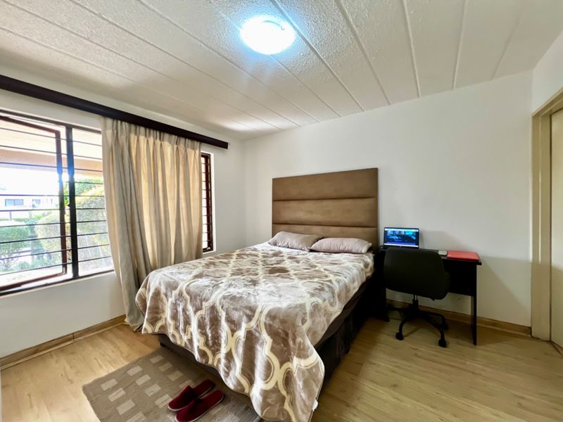 A functional bedroom featuring laminate flooring, a textured ceiling, and large windows with security bars, providing natural light and a neutral foundation.