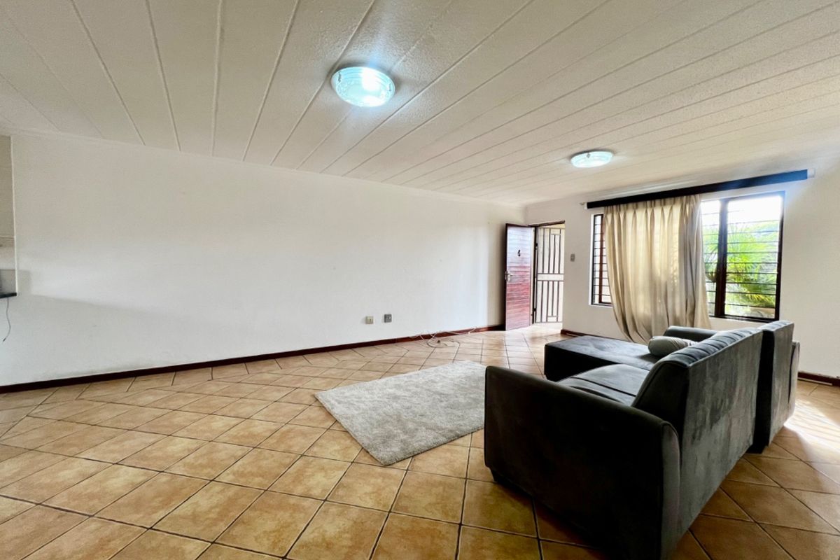 Spacious living area featuring neutral tiled flooring, flush mount lighting, and direct access to the exterior via a security gate.
