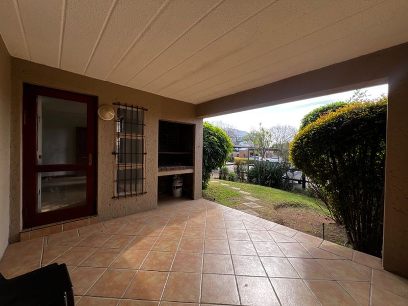 Covered patio area featuring a built-in braai, tiled flooring, and direct access to the garden, providing a functional outdoor entertainment space.