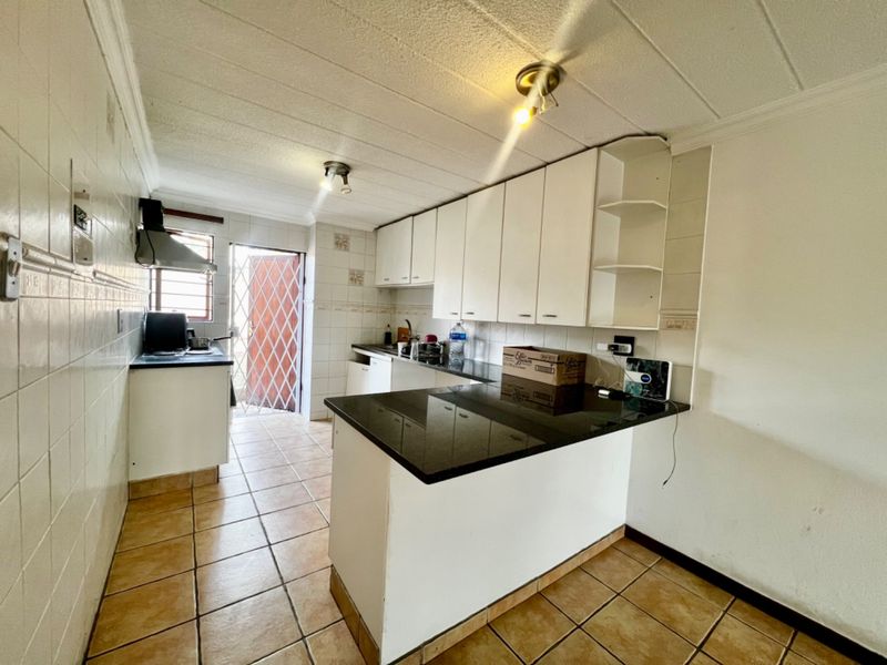 Functional kitchen featuring white built-in cabinetry, dark granite countertops, tiled flooring, and a rear exit with a security gate.