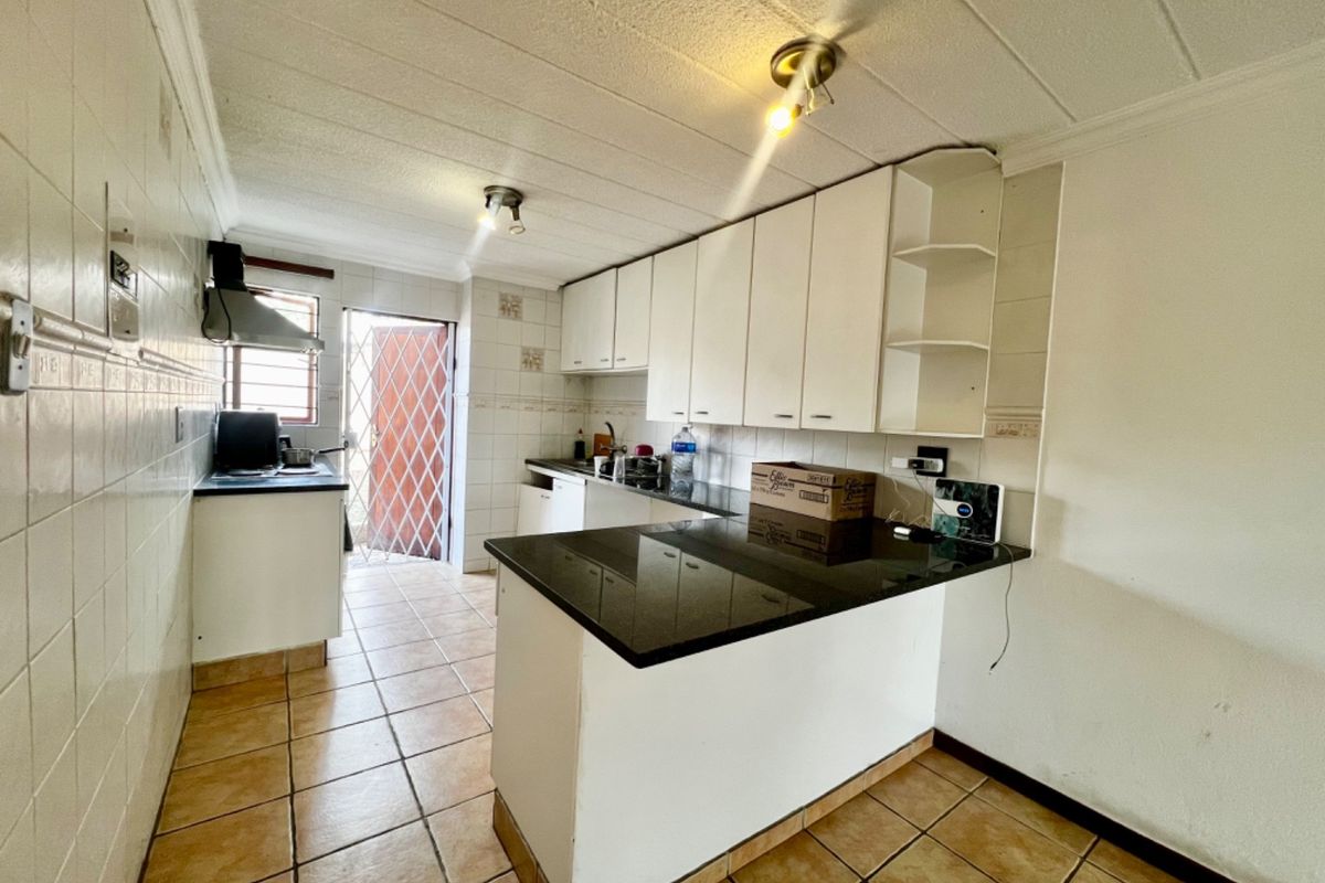 Functional kitchen featuring white built-in cabinetry, dark granite countertops, tiled flooring, and a rear exit with a security gate.