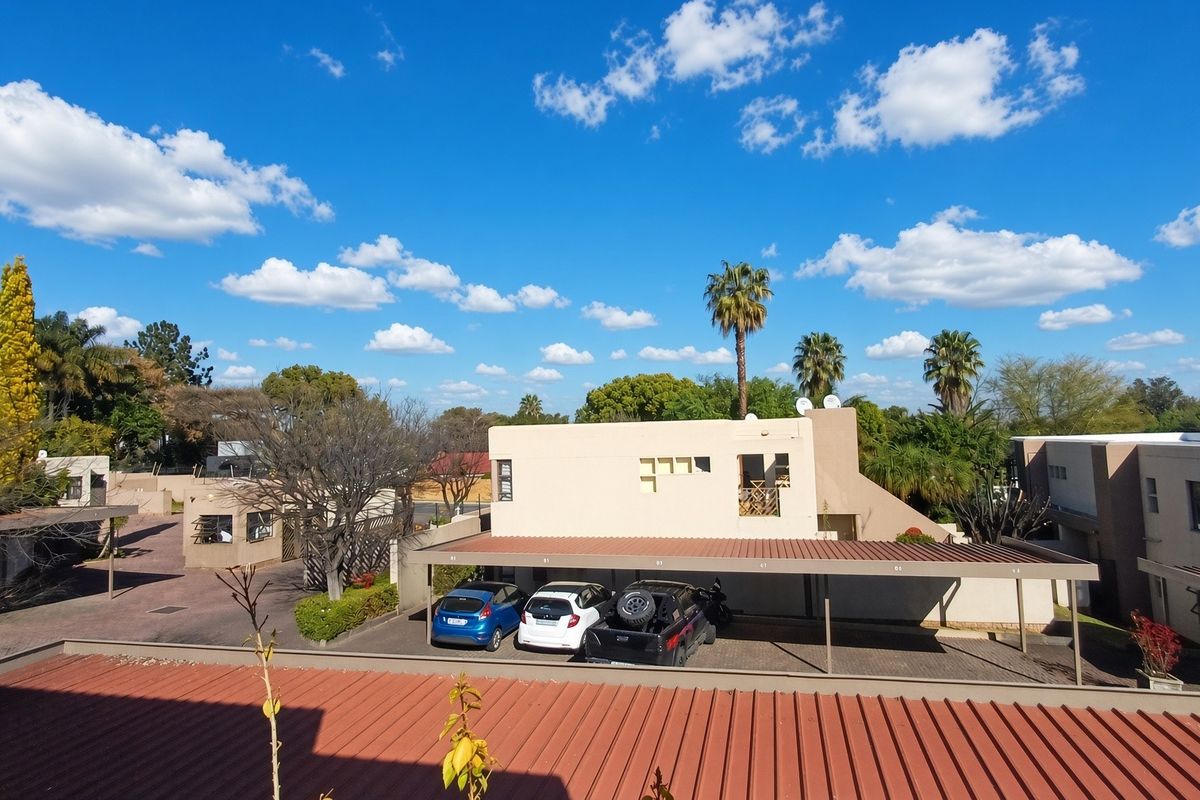 An elevated view of the apartment complex grounds, featuring covered parking bays, paved driveways, and surrounding landscaped areas under a clear blue sky.
