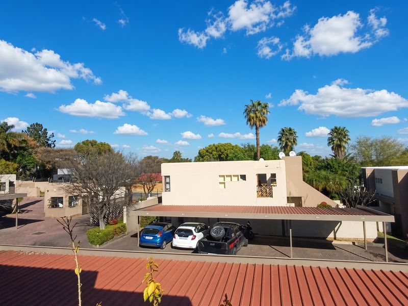 An elevated view of the apartment complex grounds, featuring covered parking bays, paved driveways, and surrounding landscaped areas under a clear blue sky.