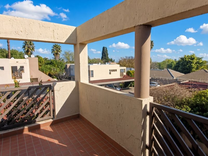 An open-air balcony featuring tiled flooring, metal balustrades, and concrete pillars, offering elevated views of the surrounding residential complex.