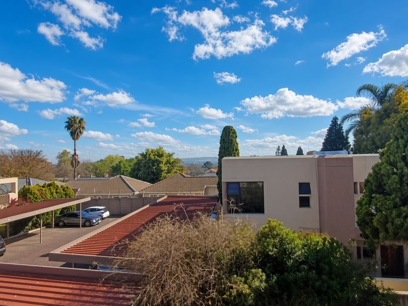 An elevated view overlooking the apartment complex grounds, featuring carports, tiled roofing, and surrounding residential landscape under a clear blue sky.