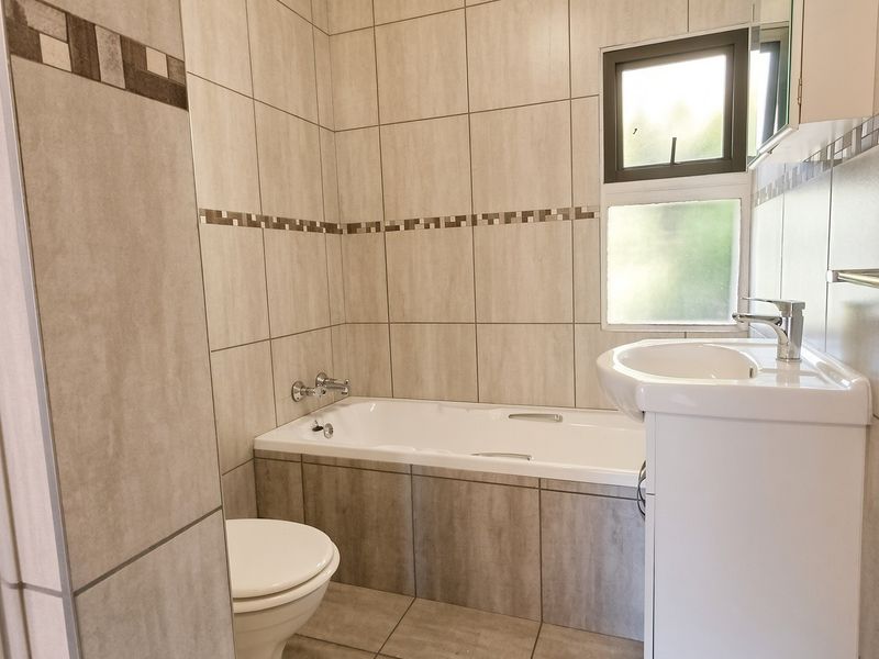 A clean, functional bathroom featuring a bathtub, pedestal basin, and neutral wall tiling with a decorative border.