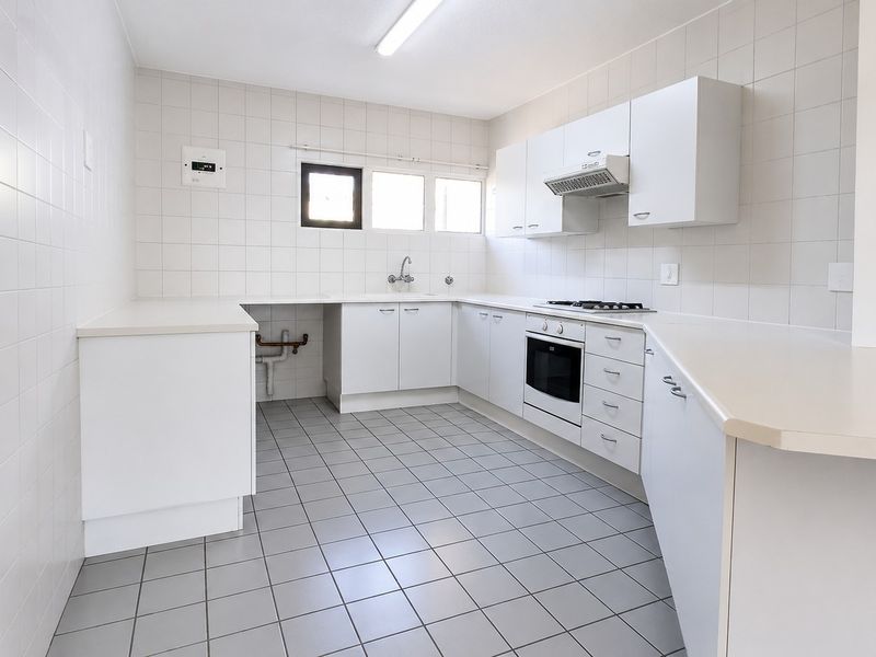 A clean, functional kitchen featuring white cabinetry, tiled walls and flooring, built-in oven, gas hob, and extractor fan, offering a blank canvas for updates.