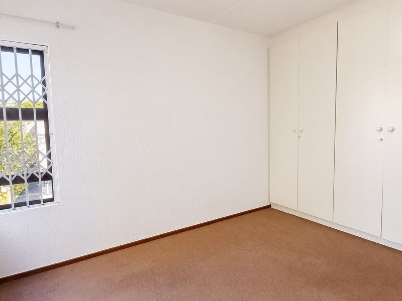 A clean, empty bedroom featuring built-in cupboards, carpeted flooring, and a window fitted with a security gate.
