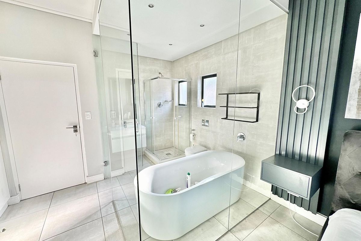 Modern en-suite bathroom featuring a sleek freestanding bathtub, glass-enclosed shower, and contemporary wall-mounted vanity with neutral tiling.