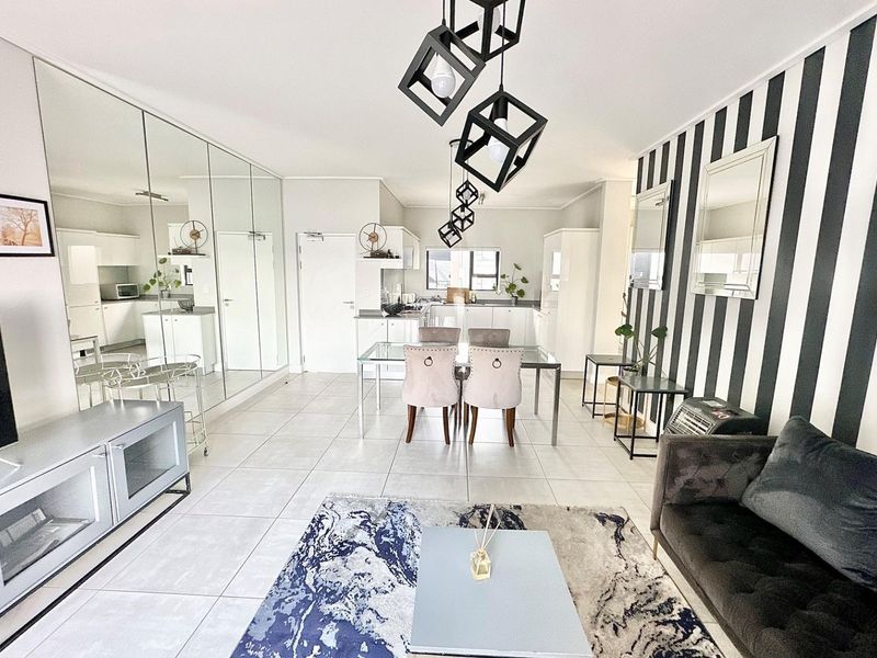 Spacious open-plan living and dining area featuring tiled floors, mirrored wall accents, and a modern kitchen with built-in cabinetry.