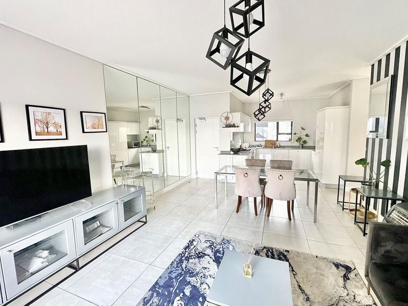 Modern open-plan living and dining area featuring sleek tiled floors, mirrored wall accents, and a contemporary kitchen with integrated cabinetry.