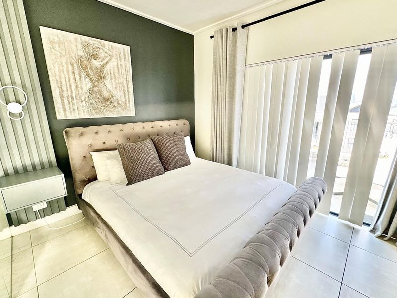 A well-maintained bedroom featuring tiled flooring, an accent wall, and large windows with vertical blinds providing natural light.