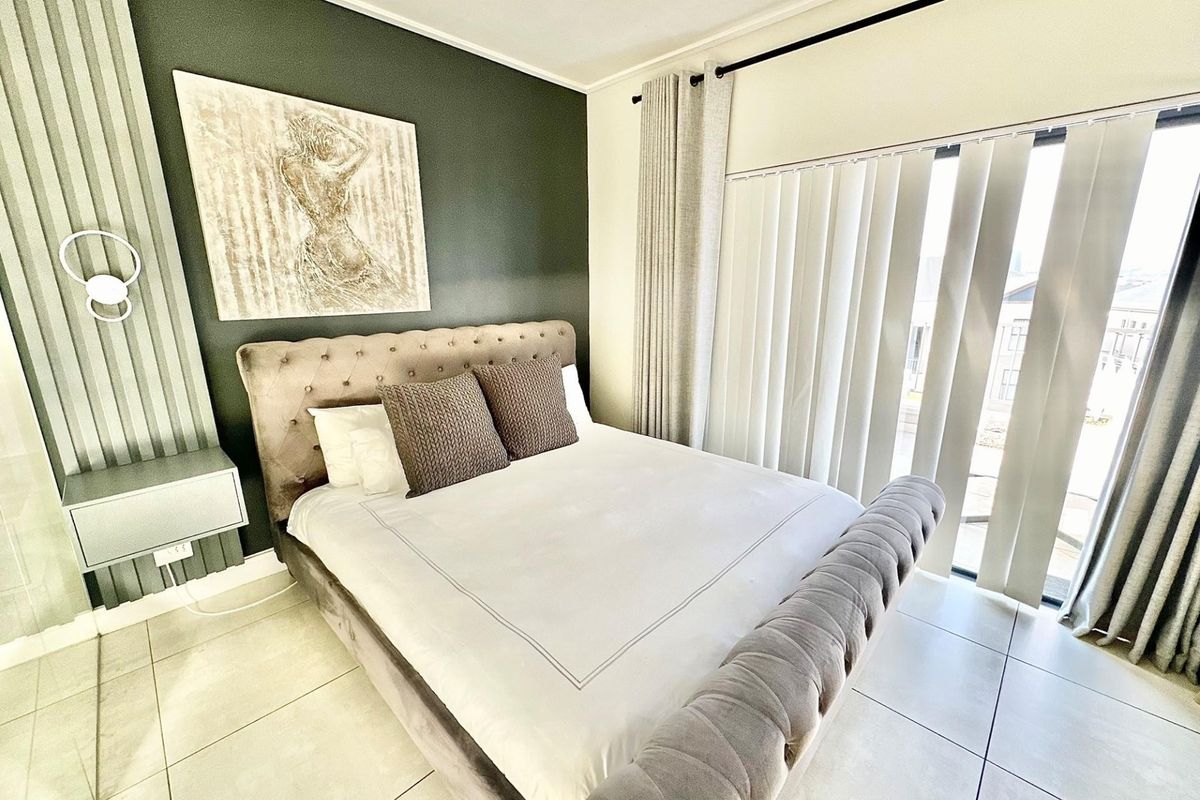 A well-maintained bedroom featuring tiled flooring, an accent wall, and large windows with vertical blinds providing natural light.