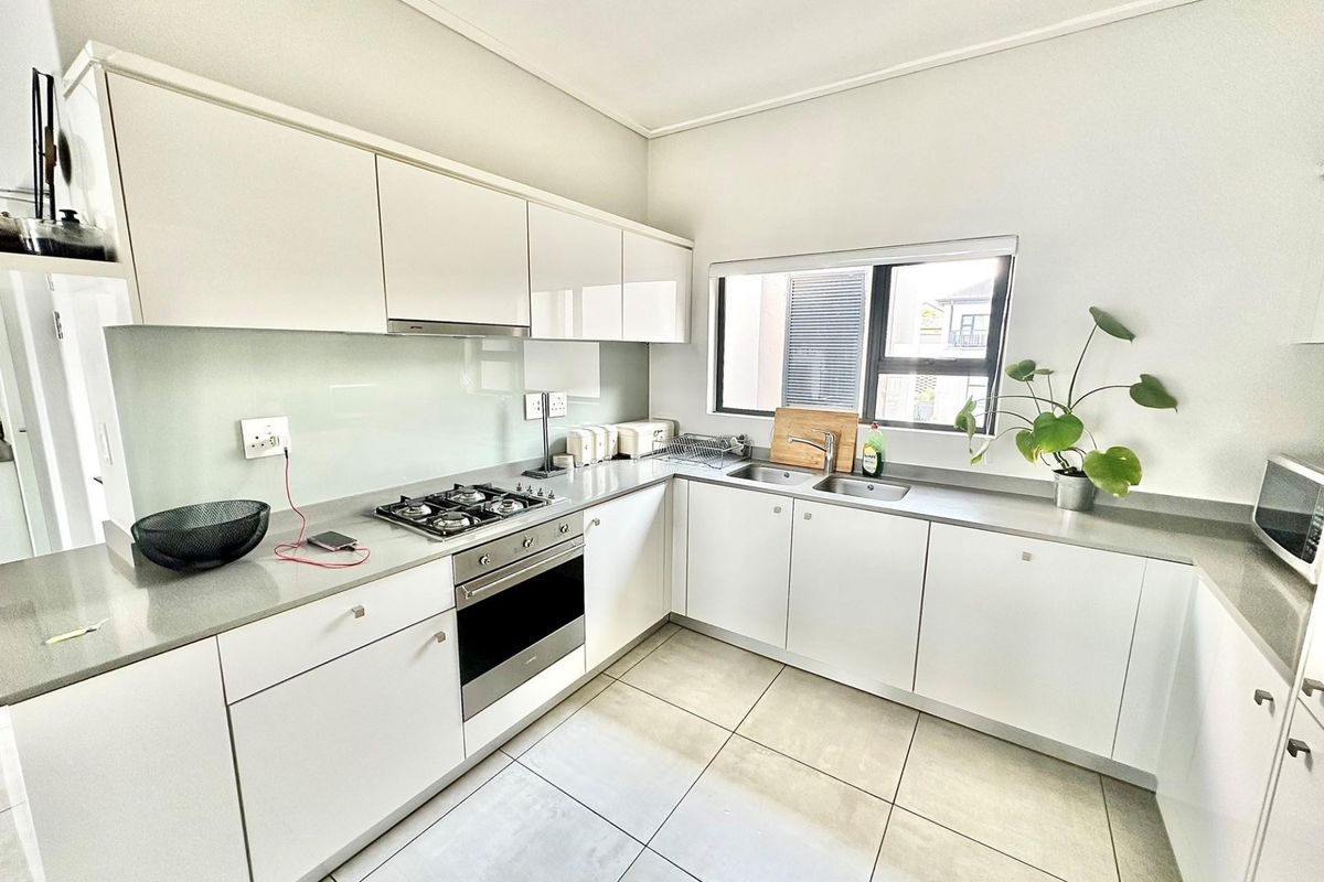 Modern kitchen featuring sleek white gloss cabinetry, stone countertops, a gas hob, built-in oven, and a glass splashback with neutral tiled flooring.