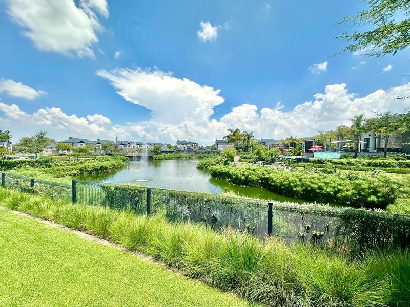 A scenic view of a landscaped estate garden featuring a central pond with a fountain and well-maintained green spaces.