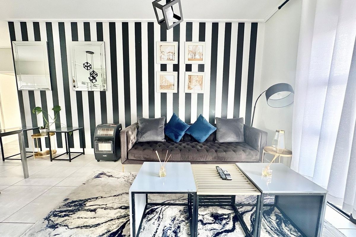 A well-maintained living room featuring modern tiled flooring and a striking black and white striped feature wall.