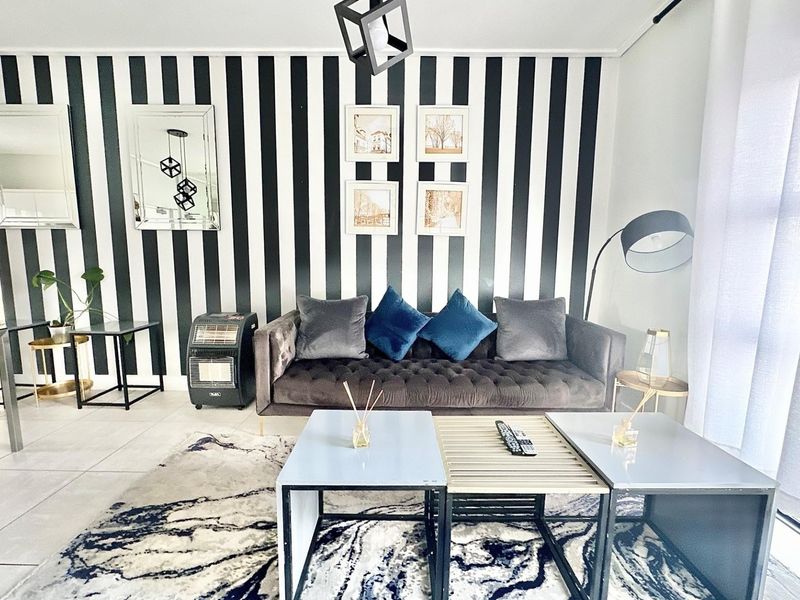 A well-maintained living room featuring modern tiled flooring and a striking black and white striped feature wall.
