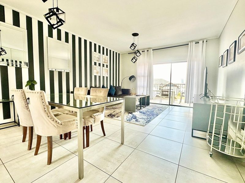 Open-plan living and dining area featuring large format floor tiles, modern pendant lighting, and a sliding glass door leading to a balcony.