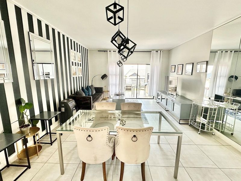 A bright open-plan living and dining area featuring tiled floors, a striking striped feature wall, and a sliding door leading to a balcony.