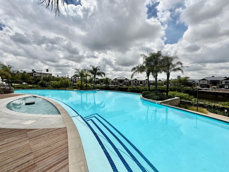 A well-maintained swimming pool area featuring integrated steps, surrounding decking, and landscaped garden elements within a residential estate setting.