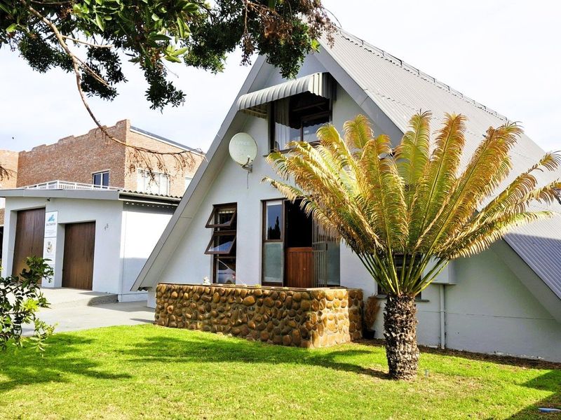 A-frame house exterior featuring a metal roof, stone-clad base, and casement windows, set within a well-maintained garden area.