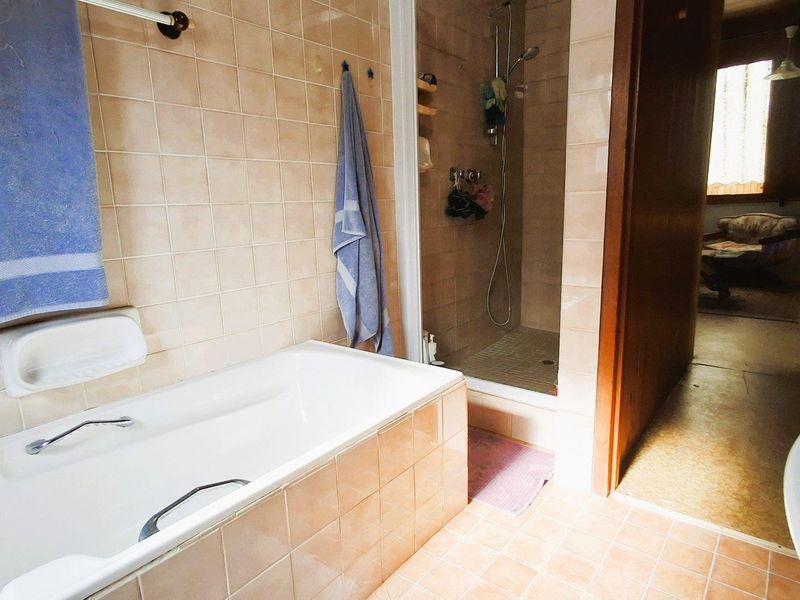 A functional bathroom featuring a built-in bathtub, a separate shower enclosure, and neutral ceramic tiling throughout.