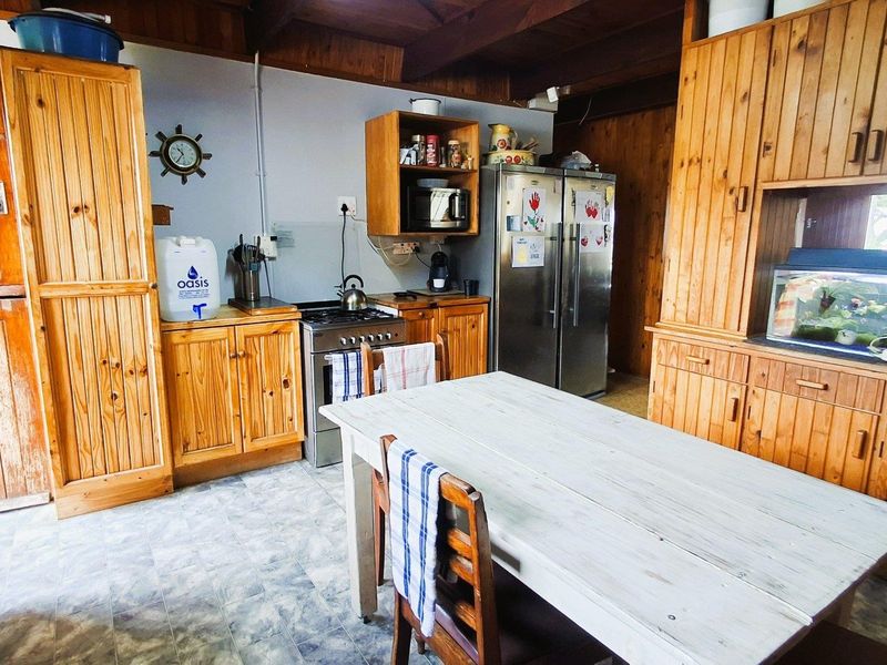 A rustic kitchen featuring extensive timber cabinetry, exposed wooden ceiling beams, and a functional layout with tiled flooring.