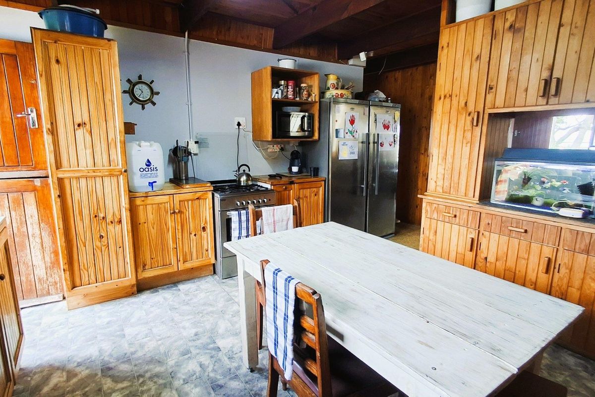 A rustic kitchen featuring extensive timber cabinetry, exposed wooden ceiling beams, and a functional layout with tiled flooring.