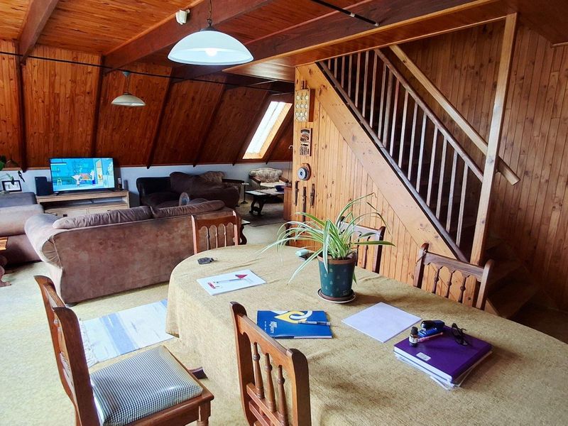 Open-plan living and dining area featuring extensive timber wall paneling, exposed beams, a built-in timber staircase, and a skylight for natural illumination.