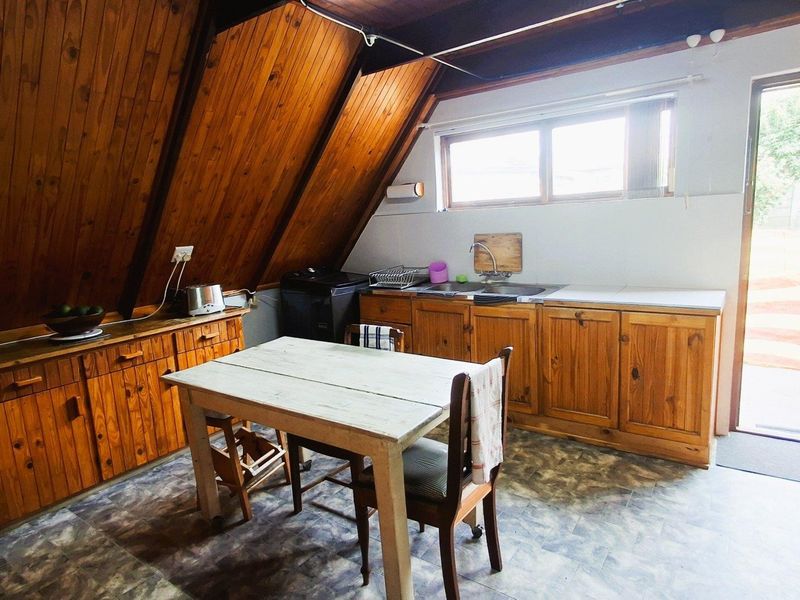 A rustic kitchen featuring wooden cabinetry, a stainless steel sink, and a distinctive sloped timber ceiling with access to an outdoor area.